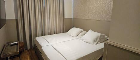 A hotel room with a bed, a desk, a chair, a television, and a curtain.