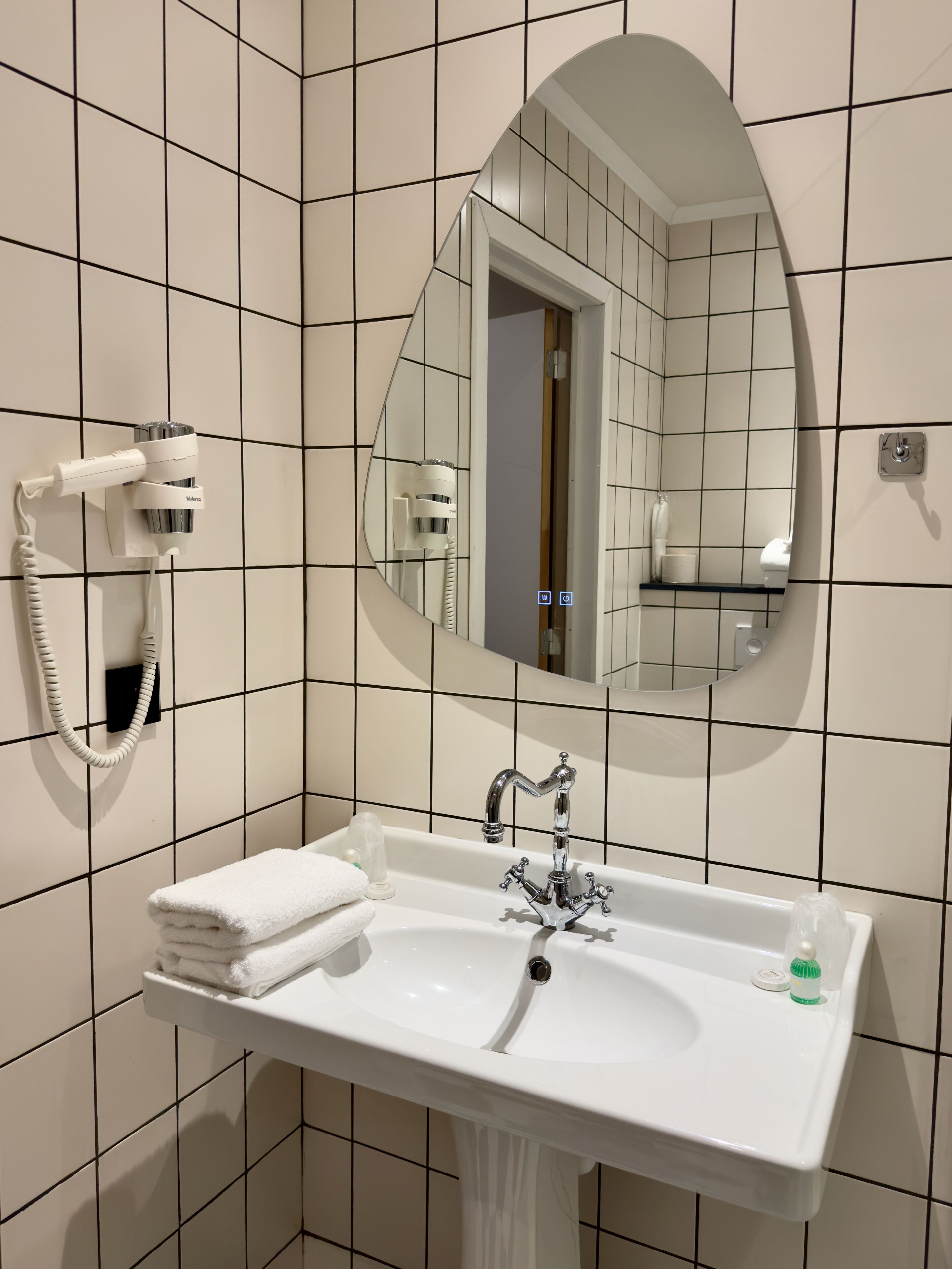 A bathroom with a white sink, a mirror, and a hairdryer mounted on the wall.