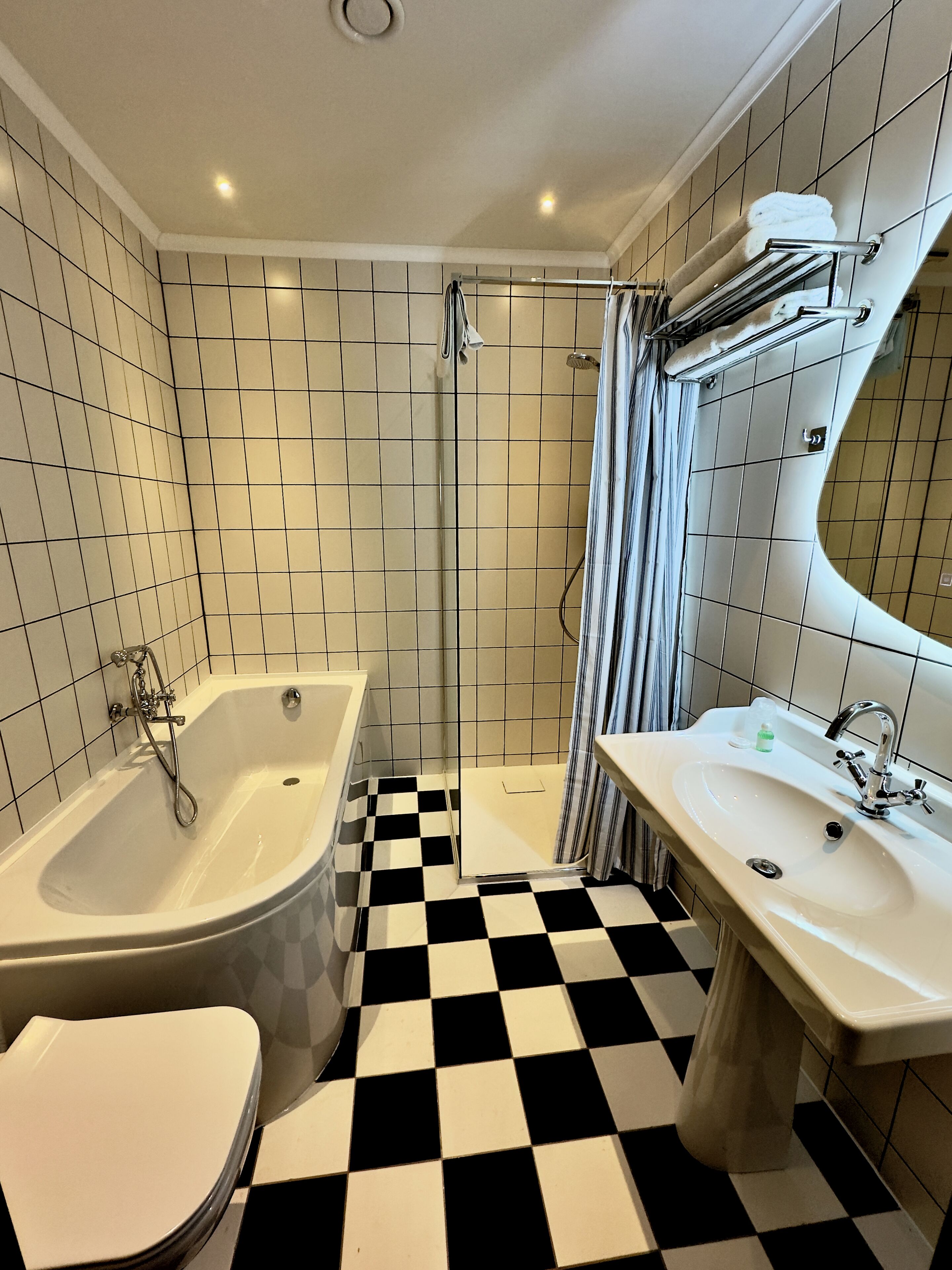 Ein Badezimmer mit Schachbrettboden, einer Badewanne, einer Dusche und einem Waschbecken.