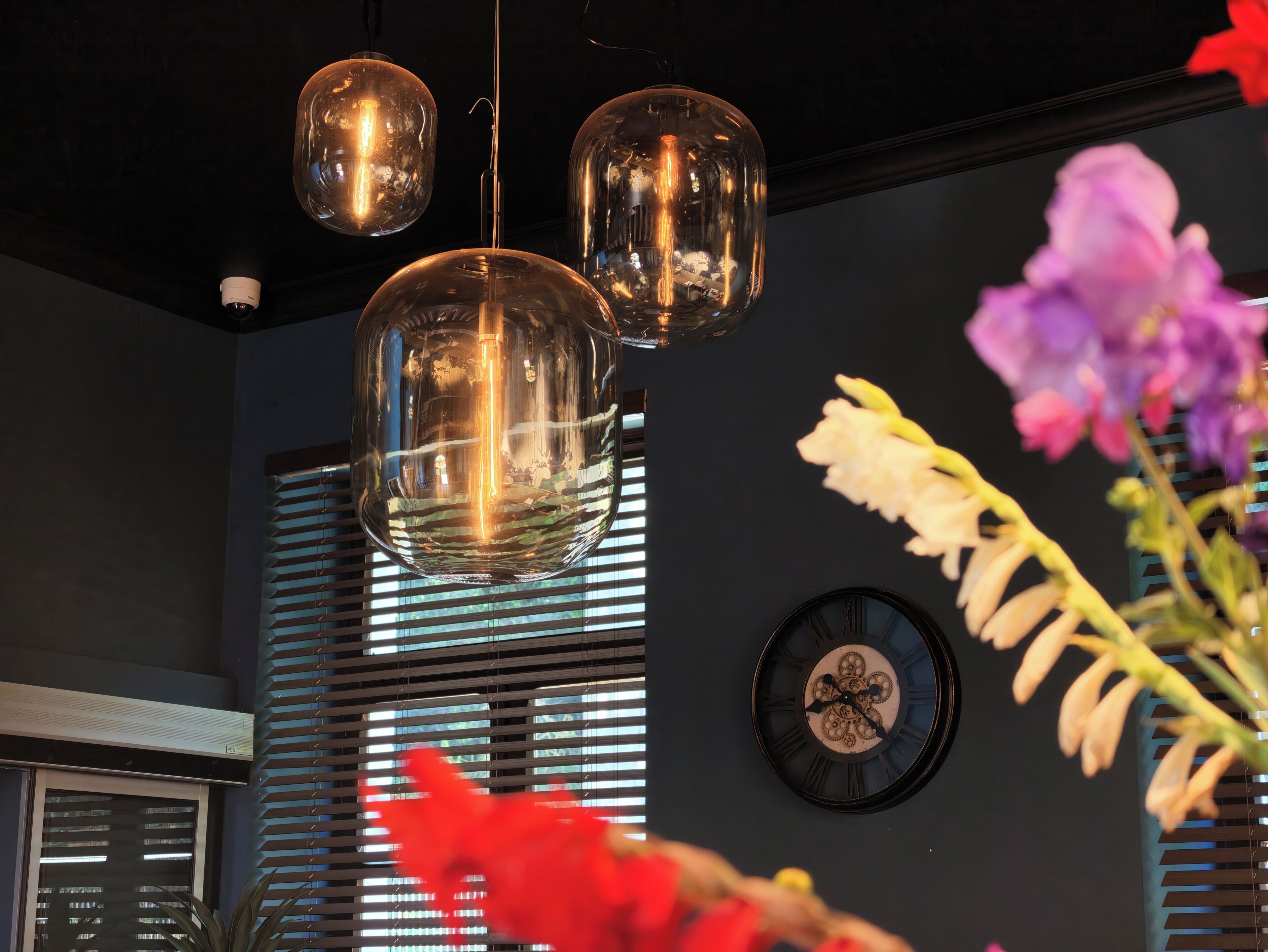 A modern interior with pendant lighting, a wall clock, and a window with blinds.