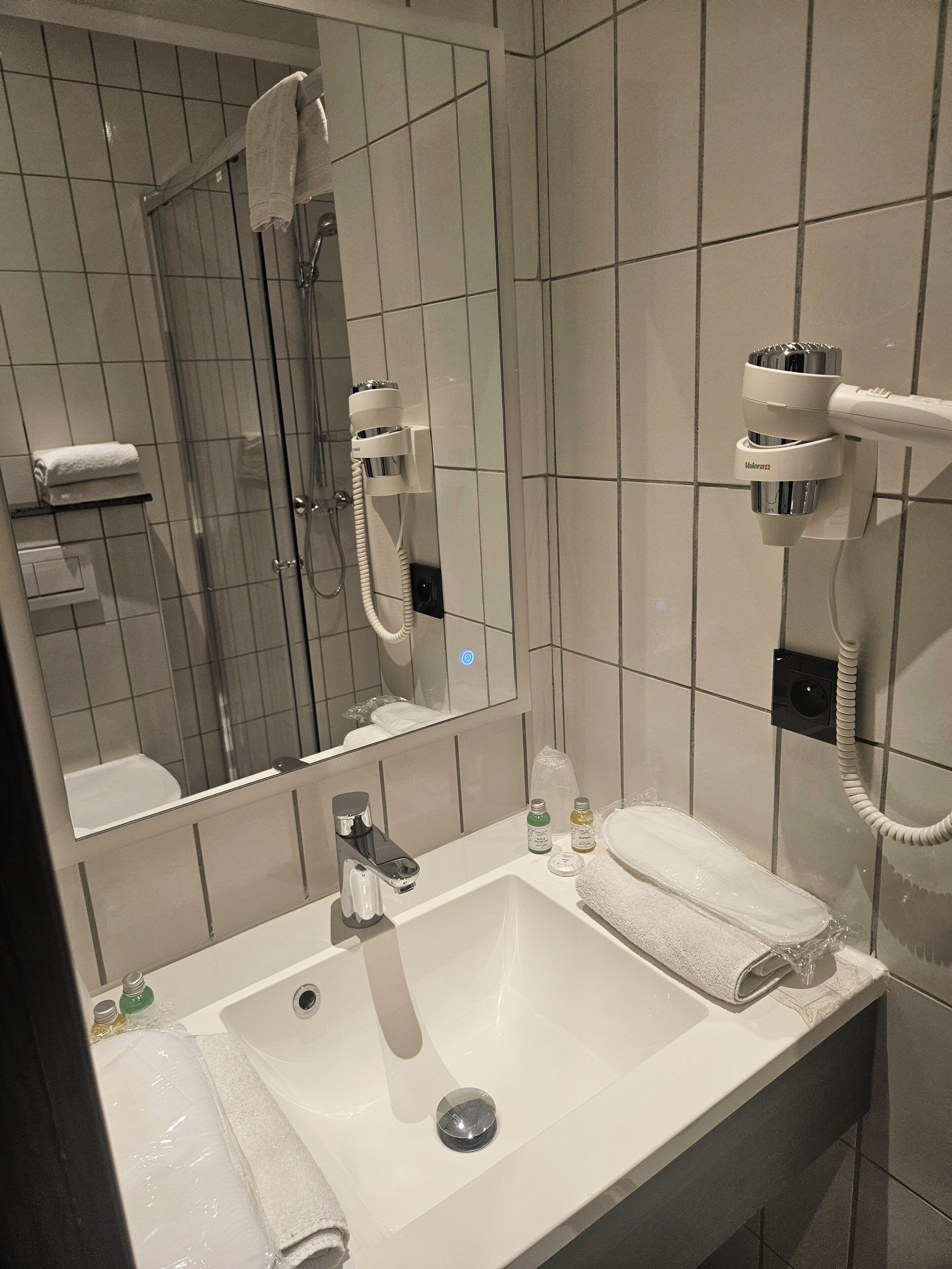 Une salle de bain avec un lavabo blanc, un miroir, un sèche-cheveux et un porte-serviettes.