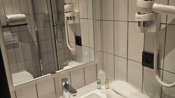 Une salle de bain avec un lavabo blanc, un miroir, un sèche-cheveux et un porte-serviettes.
