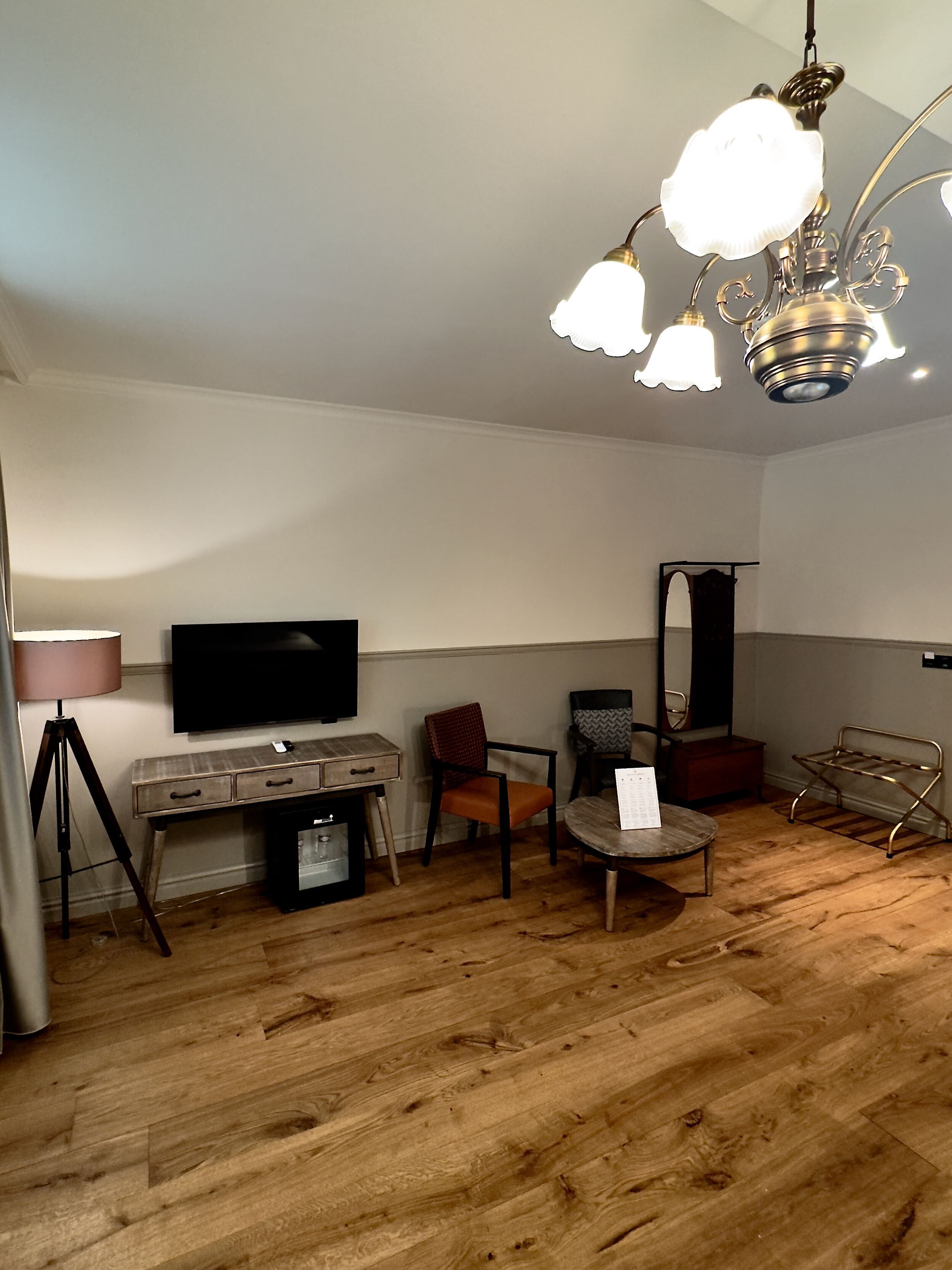 Une pièce avec un plancher en bois, une télévision, une lampe, une chaise, une petite table et un luminaire au plafond.