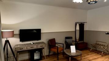 Une pièce avec un plancher en bois, une télévision, une lampe, une chaise, une petite table et un luminaire au plafond.