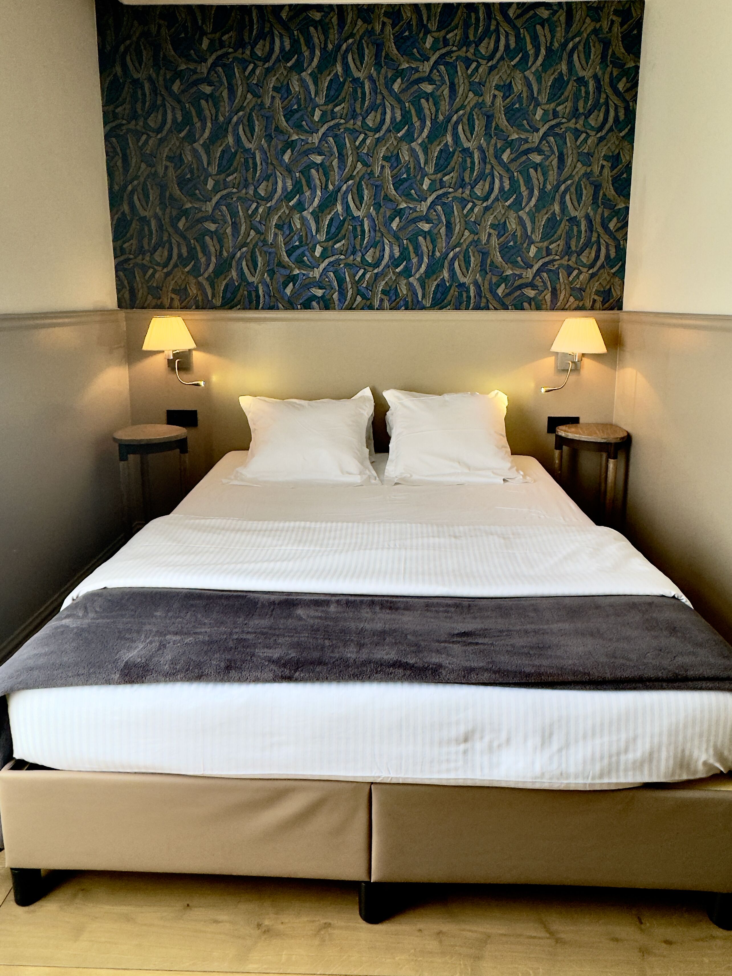 A hotel room with a large bed, two bedside lamps, and a patterned wall above the bed.