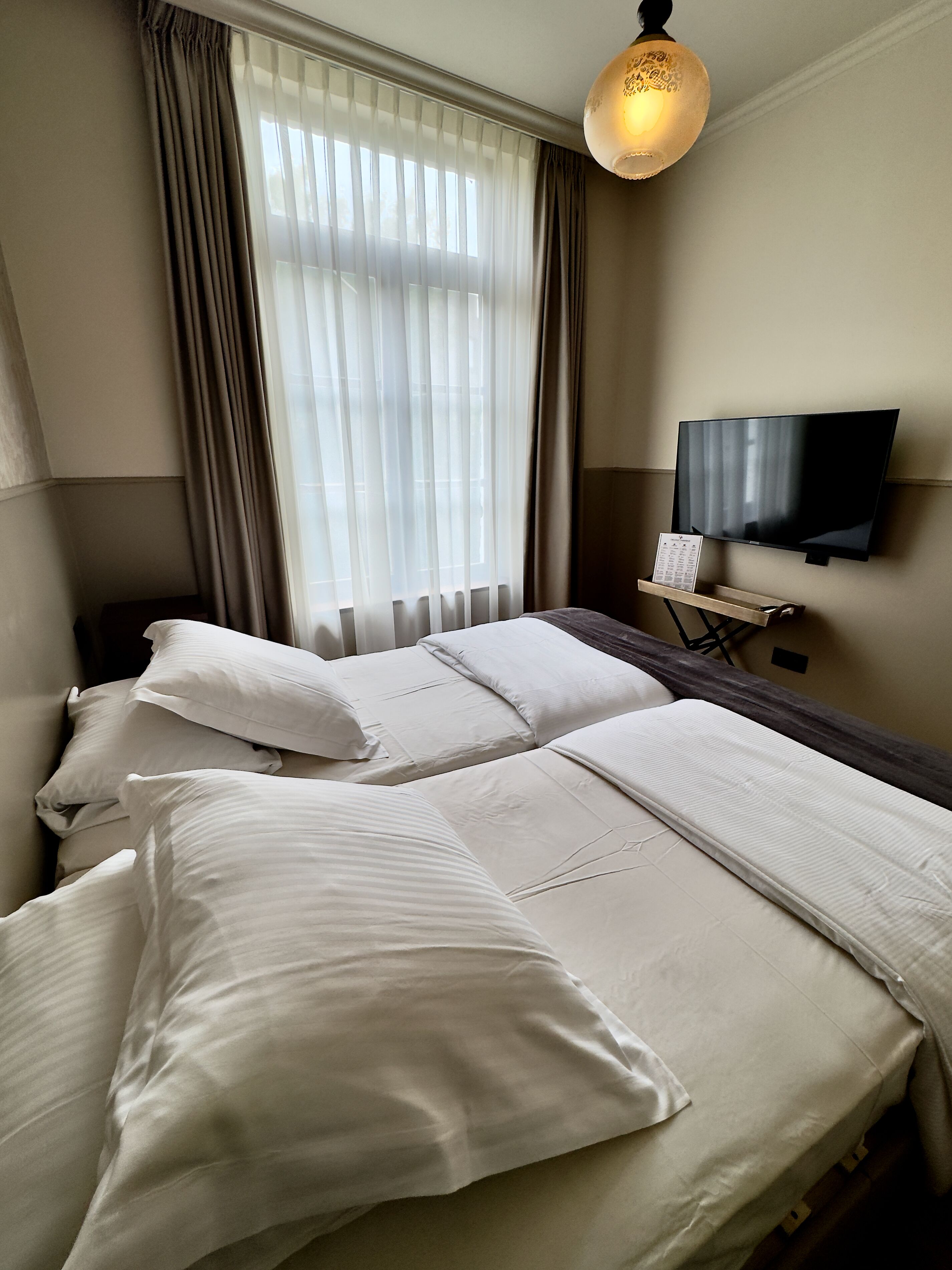 Ein Hotelzimmer mit Bett, einem Flachbildfernseher an der Wand und einem fenster mit Vorhängen.