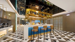 Un área de bar moderna con suelo a cuadros, una barra central y una zona de estar con taburetes.