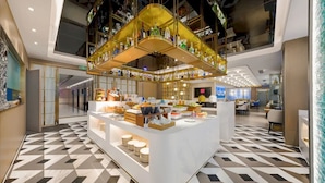 Un moderno hall de hotel con una zona de bar central, suelo con estampado geométrico y un techo alto con elementos estructurales a la vista.