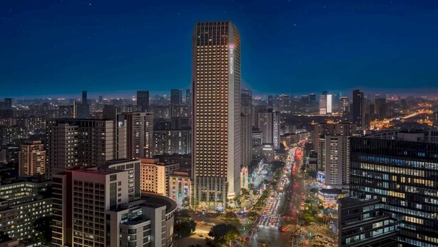 Un edificio de gran altura con fachada de diseño geométrico, rodeado de otros edificios altos y una calle concurrida abajo.