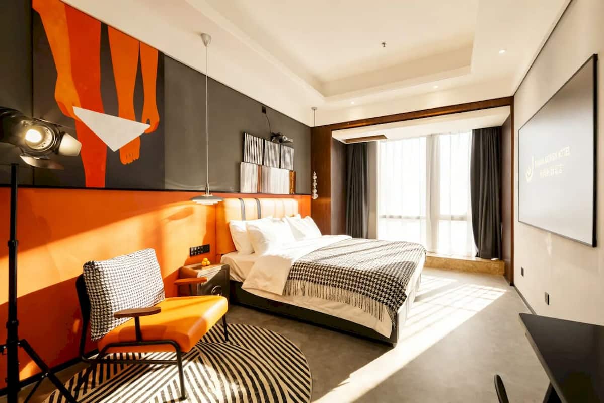 Moderni hotellihuone, jossa on suuri sänky, työpöytä, tuoli, televisio ja suuri ikkuna, jossa on verhot.
