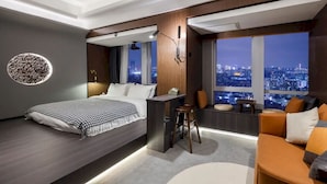 Habitación de hotel moderna con una cama grande, un escritorio, un sofá y vistas a la ciudad.