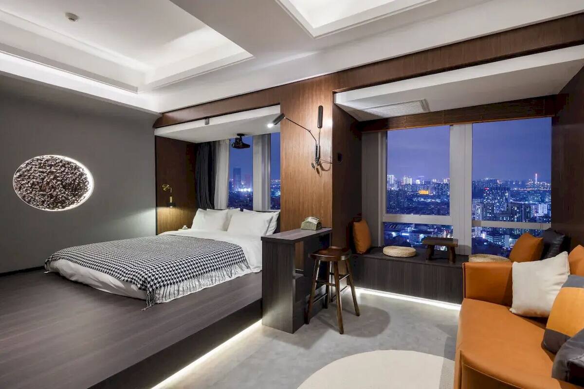 Moderni hotellihuone, jossa on suuri sänky, työpöytä, sohva ja näkymä kaupunkiin.