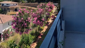 A balcony with a view of a hillside, a palm tree, and a building with a tiled roof. - Between sea and mountains, spacious, quiet apartment with superb views. (Alata)