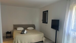 A bedroom with a bed, a bedside table, a TV, and a window with curtains. - Between sea and mountains, spacious, quiet apartment with superb views. (Alata)