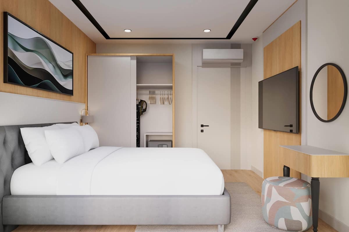 Un dormitorio moderno con cama, televisión, armario y baño visible a través de una puerta abierta.