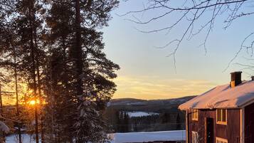 A snow-covered landscape with a wooden cabin, a clear sky, and a sunset.