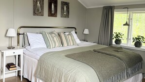 Une chambre avec un grand lit, deux tables de chevet, une fenêtre avec des rideaux et une vue sur la verdure.