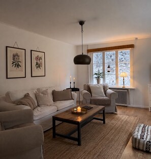 A living room with a sofa, armchairs, a coffee table with candles, a hanging light, and a window with frost. - Unique accommodations close to nature in northern Sweden (Gran)