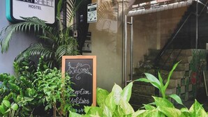 De ingang van een hostel met een bord waarop 'HOLY SHEET HOSTEL' staat, een welkomstbord, een receptiebalie en een trap die naar binnen leidt.