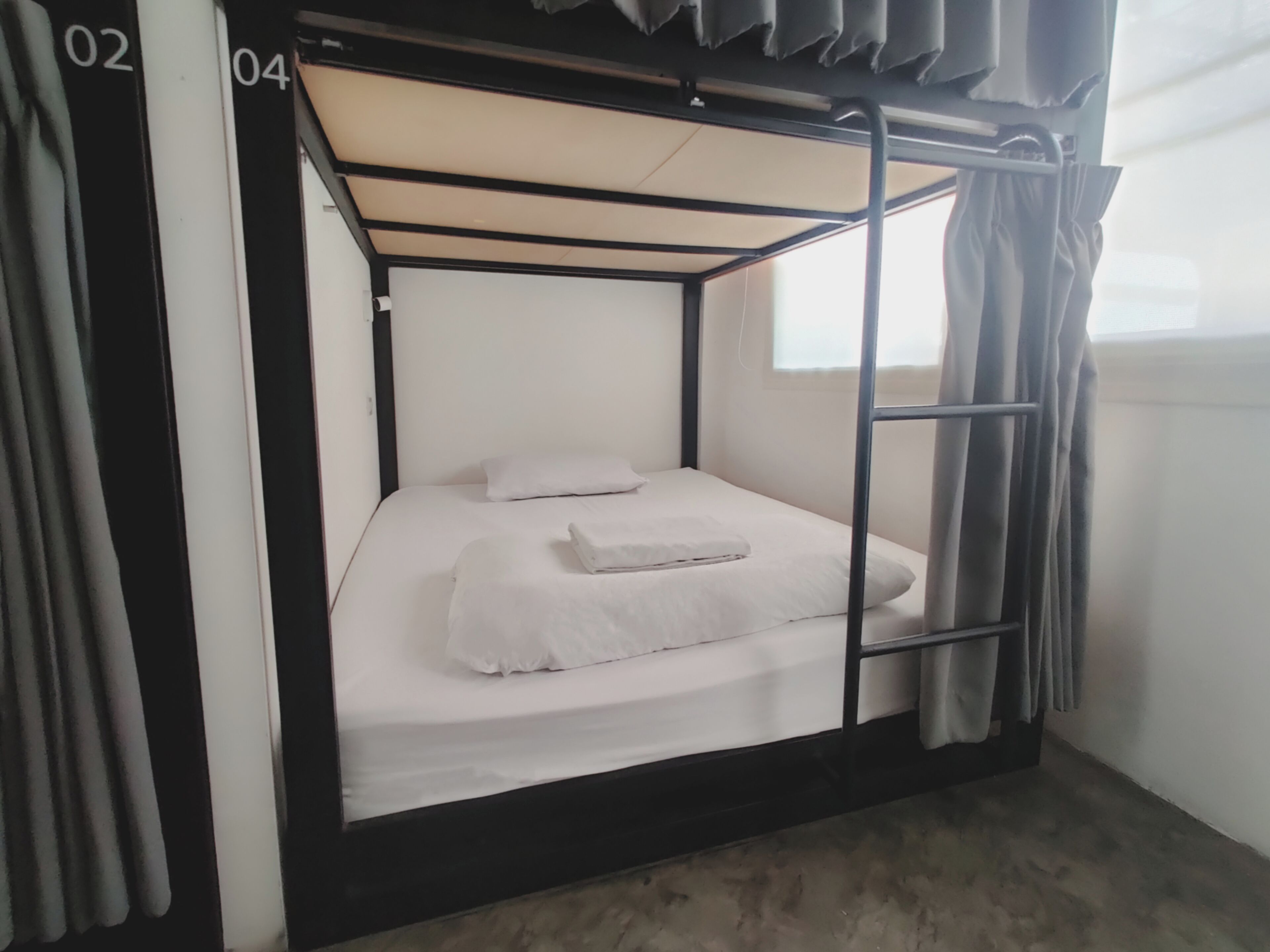 Una cama litera con estructura metálica, ropa de cama blanca y una ventana con cortinas.