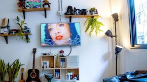 Een woonkamer met een televisie, boekenkasten vol boeken en spelletjes, een gitaar en een bank.