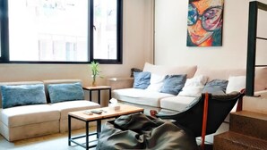 Een woonkamer met een bank, een salontafel, een relaxstoel, een klein tafeltje met een plant en een trap.
