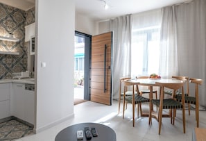 Une cuisine moderne avec des meubles blancs, un coin repas doté d’une table ronde et de chaises, et une grande fenêtre agrémentée de rideaux.