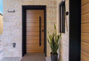 Entrada con muro de piedra, puerta de madera, planta en maceta y pequeña ventana.