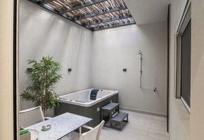 A modern bathroom with a hot tub, a small table, and a potted plant.
