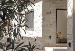 Un bâtiment en pierre avec une porte, des plantes en pot et un banc.