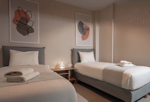 Hotellihuone, jossa on kaksi sänkyä, yöpöytä lampun kanssa ja kaksi kehystettyä taideteosta seinällä.