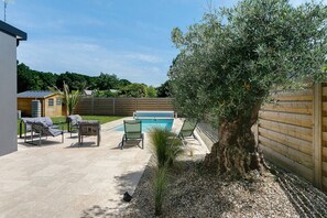 A backyard with a swimming pool, two lounge chairs, a small palm tree, and a wooden fence.