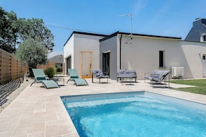 A swimming pool with lounge chairs, a wooden fence, and a modern building with a door and windows.