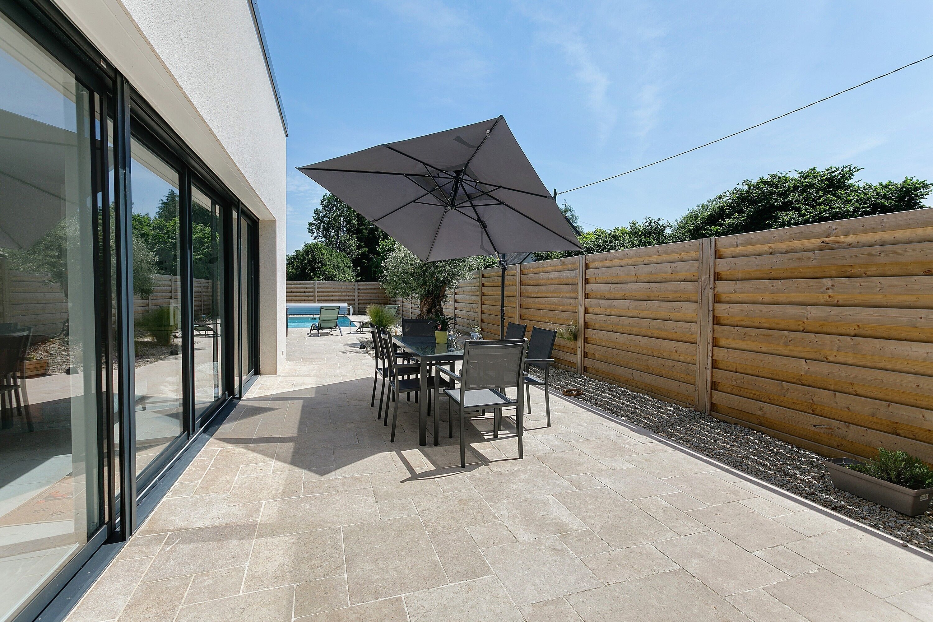 Eine Terrasse mit Tisch und Stühlen, einem großen Sonnenschirm und einem Holzzaun.