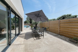 Eine Terrasse mit Tisch und StĂŒhlen, einem groĂen Sonnenschirm und einem Holzzaun.