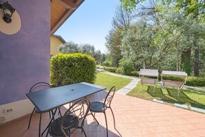 Un patio al aire libre con mesa y sillas, una zona cubierta y un sendero que conduce a un jardín.