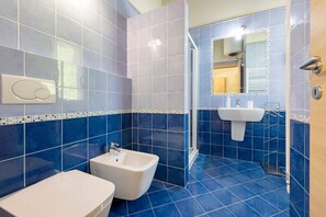 Un baño con azulejos azules, un lavabo, un bidé y una ducha con mampara de vidrio.