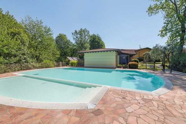 Una piscina con baldosas de piedra, una zona cubierta y una casa al fondo.