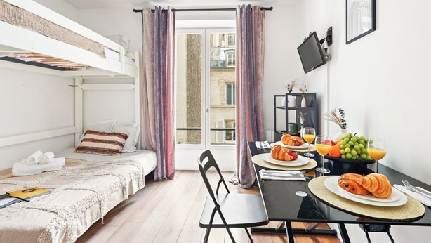 A compact room with a bunk bed, a dining table with breakfast, and a large window with curtains.
