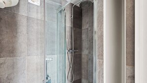 A modern shower with a glass door, a handheld showerhead, and a wall-mounted faucet.