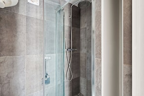 Una ducha moderna con puerta de vidrio, cabezal de ducha de mano y grifo empotrado.