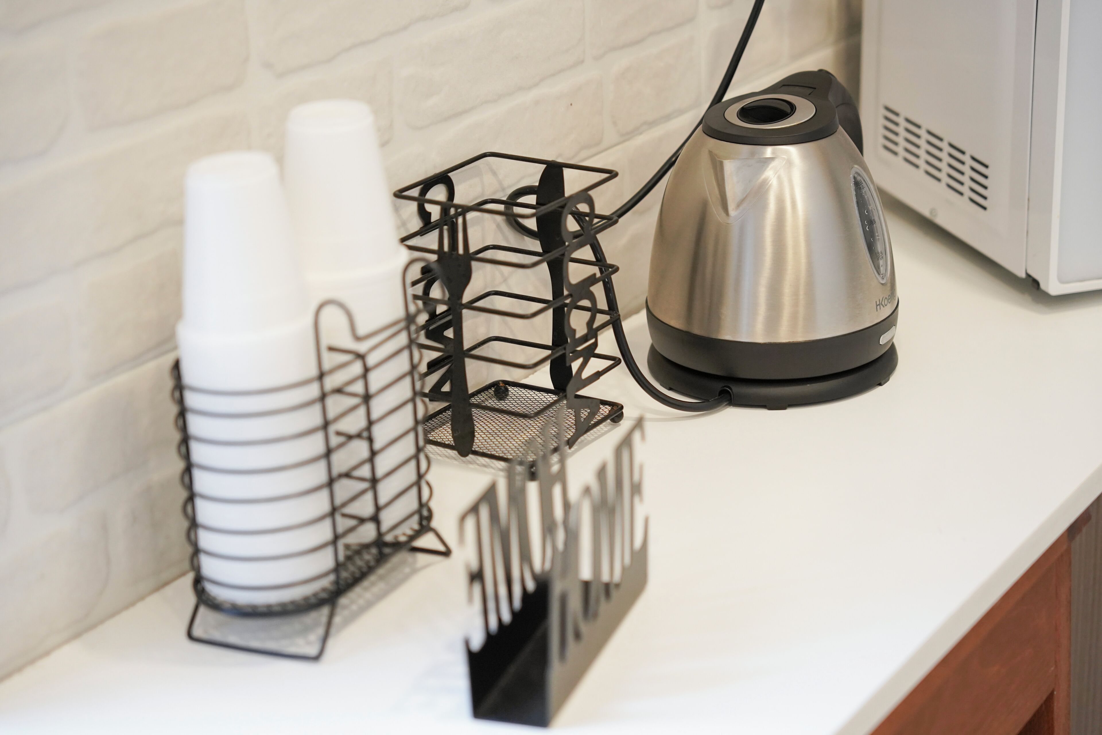 A kitchen counter with a coffee maker, a metal rack with cups, and a sign with the word 'HOME'.