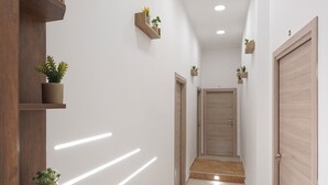 A hallway with wooden shelves holding potted plants, a tiled floor, and a wooden door at the end. - Napoli Incanto (Naples)