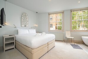 Ein Schlafzimmer mit Bett, Nachttisch, Stuhl und einem großen Fenster.