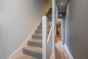 Eine Treppe mit Teppichstufen und weißen Geländern, die zu einem Raum mit Holzboden und strukturierter Wand führt.
