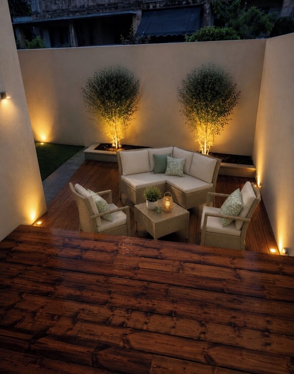 A patio with a wooden table and four chairs, two potted plants, and a small table with a candle.