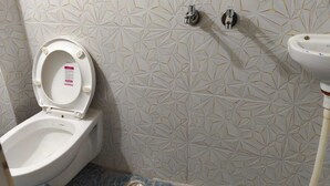 A bathroom with a toilet, a sink, and a wall-mounted faucet. - Shree Rudraksha Home Stay (Varanasi)