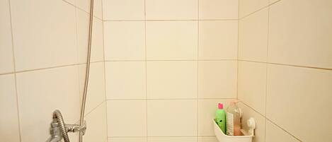 Una ducha con cabezal de ducha de mano, grifo empotrado en la pared y un pequeño estante con artículos de aseo.