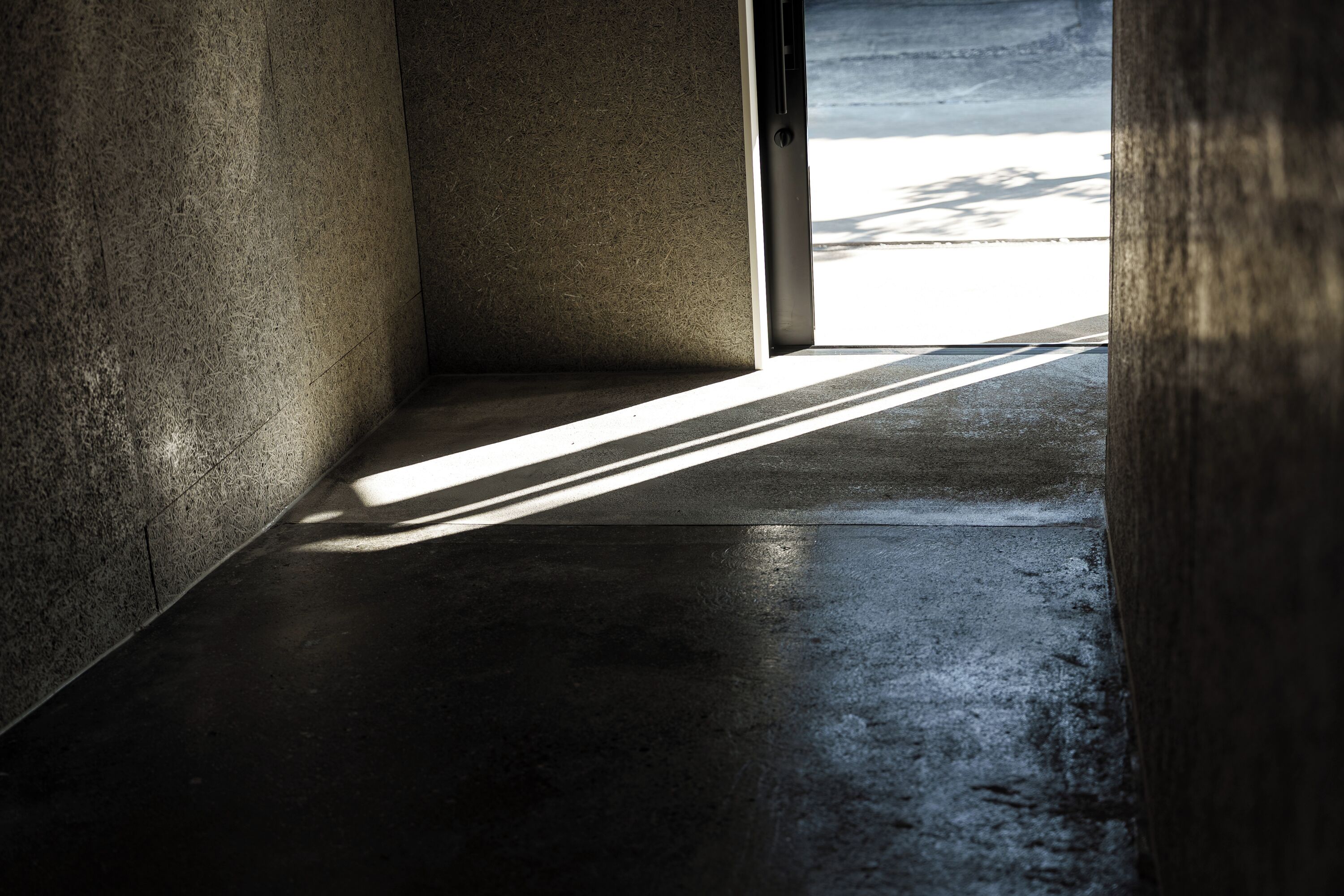 A corridor with a concrete floor and walls, leading to an open area with a view of the sky.