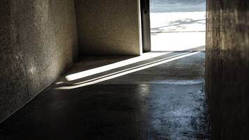 A corridor with a concrete floor and walls, leading to an open area with a view of the sky.